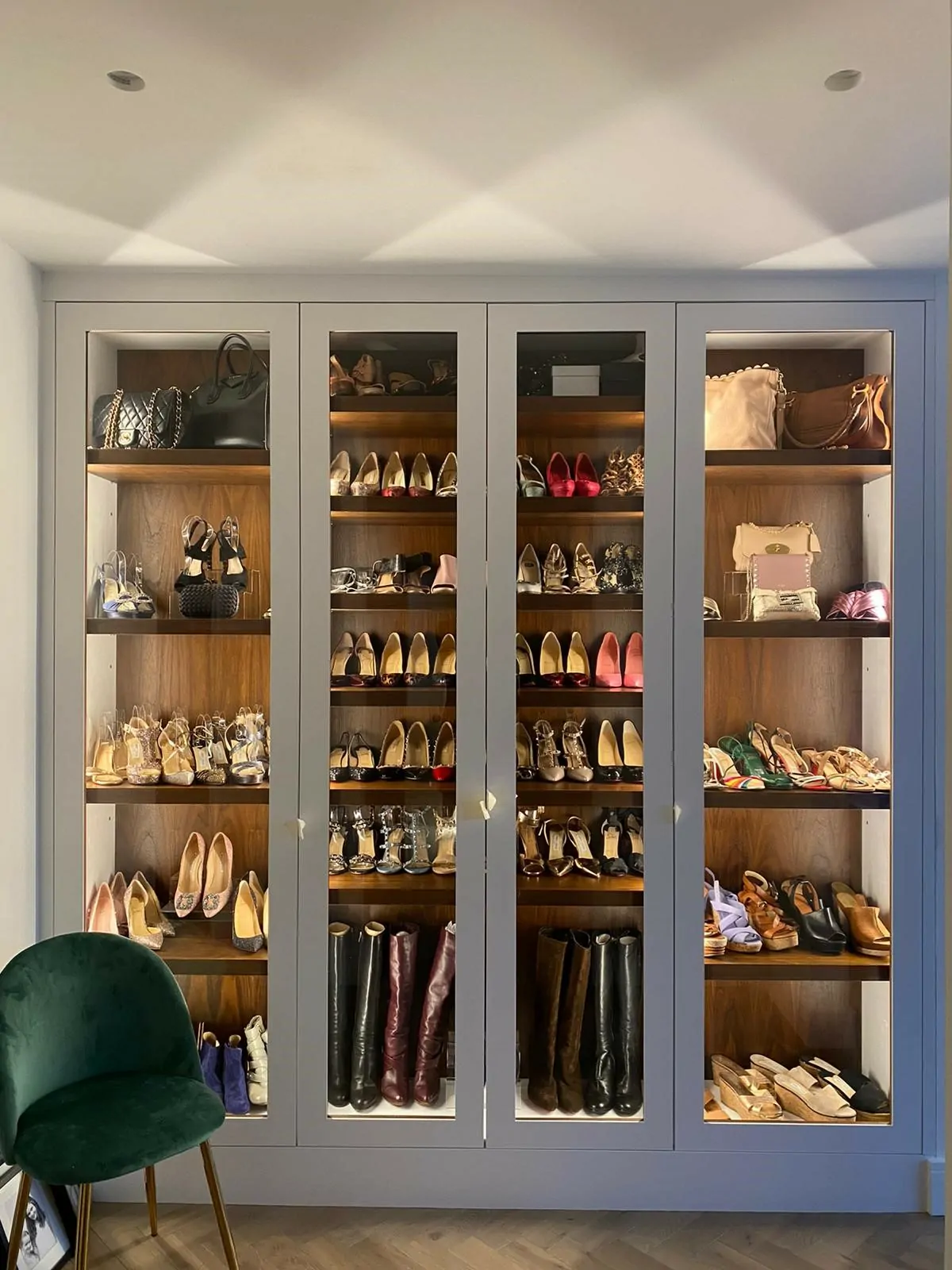 A large grey cabinet full of shoes with glass viewing door and lighting inside